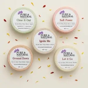 Five pure & natural body essentials shower steamers labeled clear it out, soft power, let it go, ignite me, and ground down, arranged on a white background in a stylized product display.