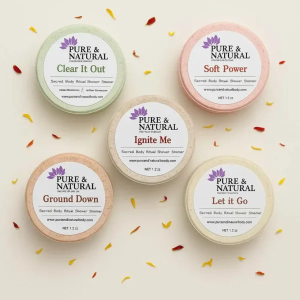 Five Pure & Natural Body Essentials shower steamers labeled Clear It Out, Soft Power, Let It Go, Ignite Me, and Ground Down, arranged on a white background in a stylized product display.