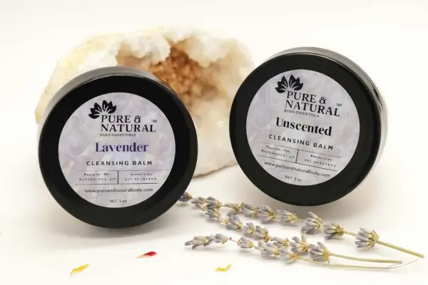 Two pure & natural body essentials cleansing balm jars in lavender and unscented varieties, displayed in front of a white crystal geode with sprigs of dried lavender on a white background.