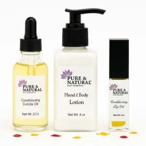 Pure & natural body essentials products including conditioning cuticle oil, unscented hand & body lotion, and conditioning lip oil displayed on a clean white background with scattered dried flower petals.
