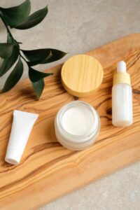 Flat-lay of eco-friendly natural skincare products including glass jars, wooden brushes, and organic oils on a white background with greenery.
