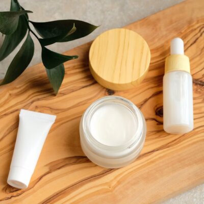 Flat-lay of eco-friendly natural skincare products including glass jars, wooden brushes, and organic oils on a white background with greenery.
