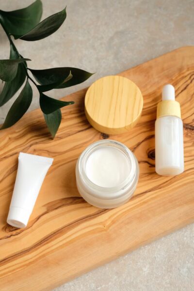 Flat-lay of eco-friendly natural skincare products including glass jars, wooden brushes, and organic oils on a white background with greenery.